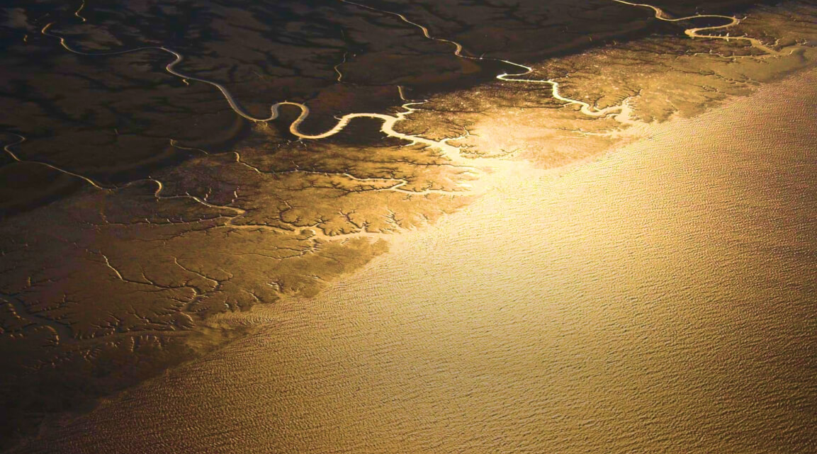 Aerial view of an Arctic landscape at sunrise in shades of gold and ochre with a network of tributaries leading to the sea