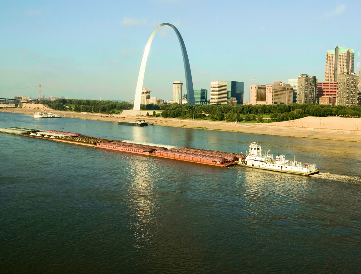 A shipping boat pushing barges down the Mississippi River near the Gateway Arch in St. Louis, Missouri